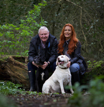 Father and daughter with black and white Labradors sat down in lush green woodland 